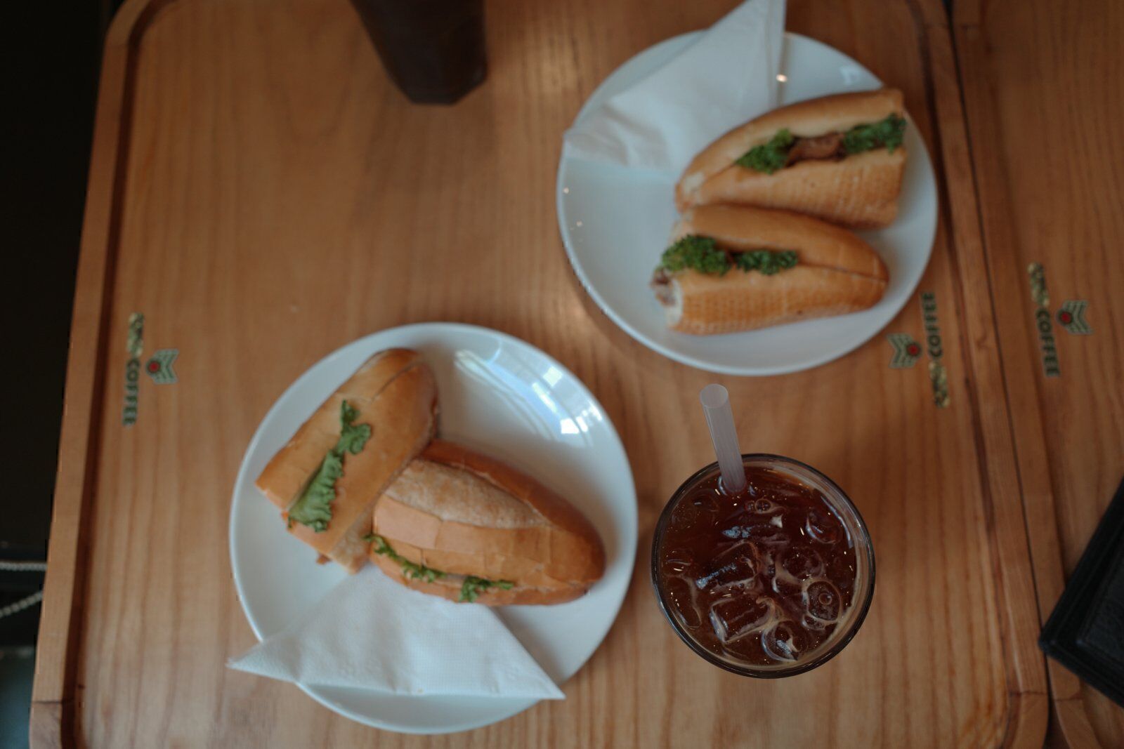 Two banh mi on plates with an iced coffee served on a wooden tray at a Da Nang cafe