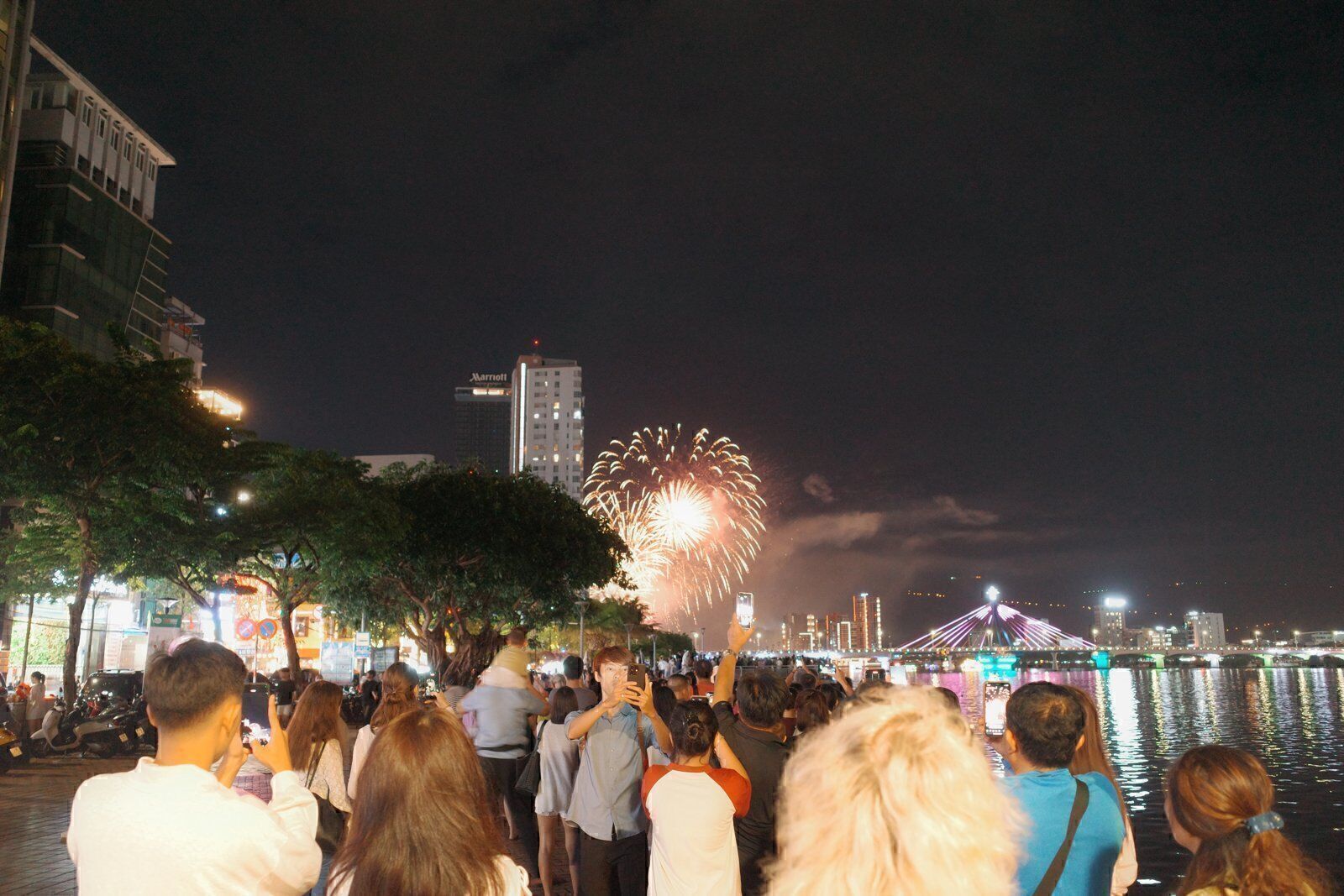 Crowd on the Han River promenade watching fireworks burst over the bridges of Da Nang at night