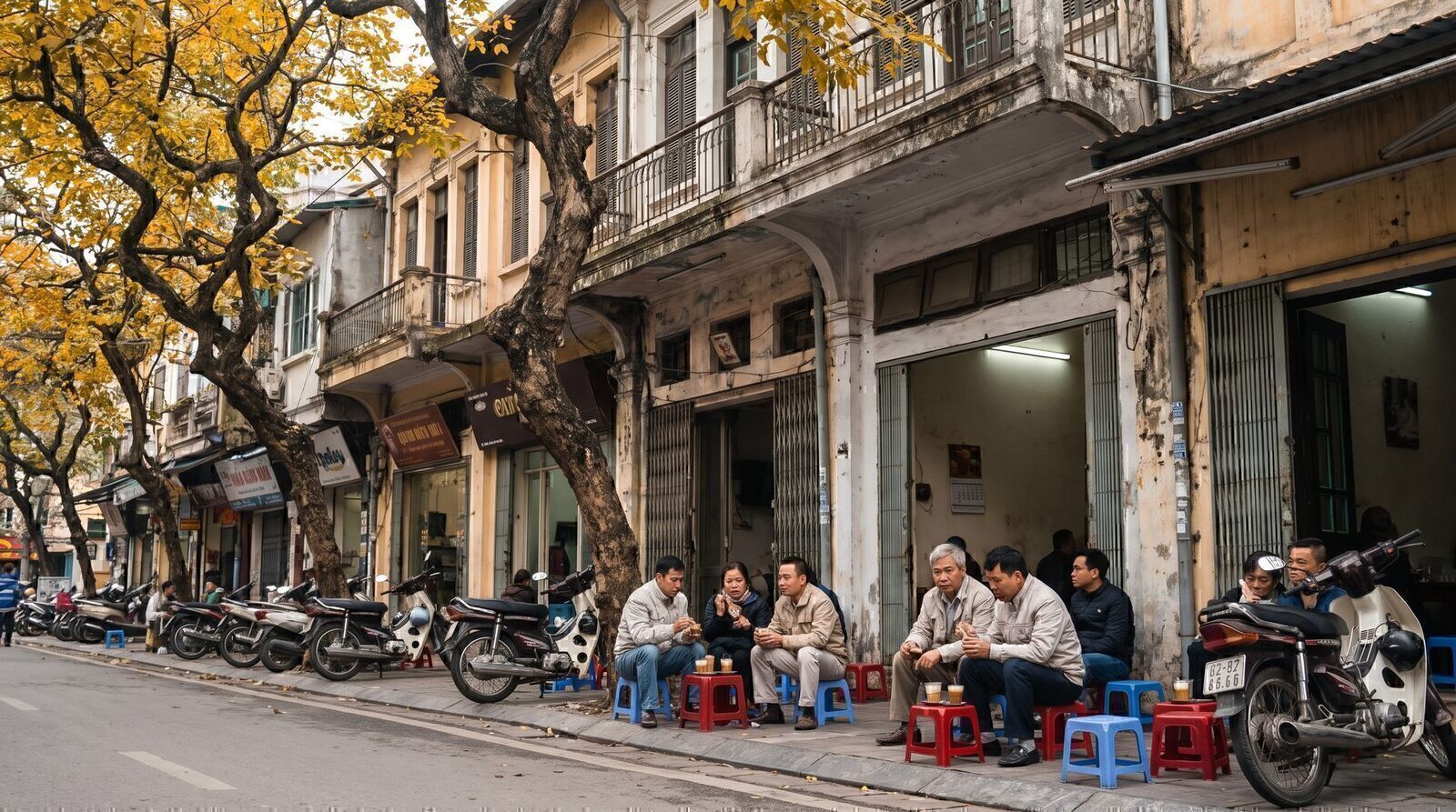 Hanoi Old Quarter street in October autumn with golden leaves and locals drinking coffee on low stools