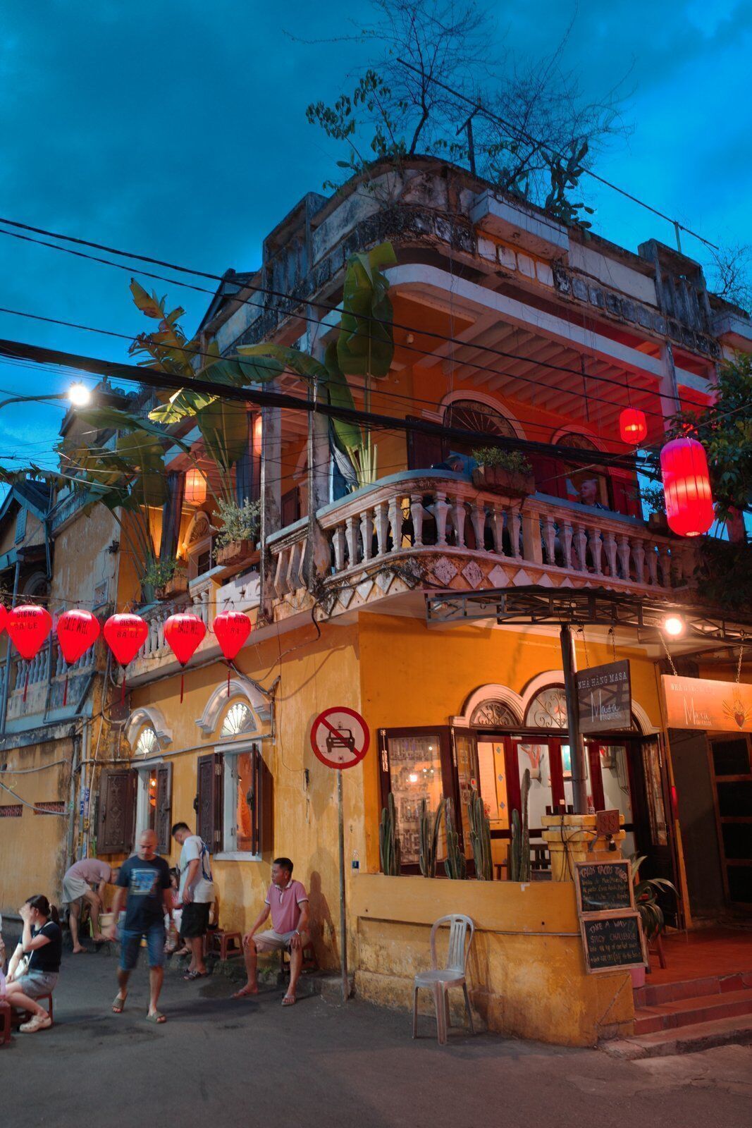 Yellow heritage house with balcony and lanterns at dusk on a quiet Hoi An side street