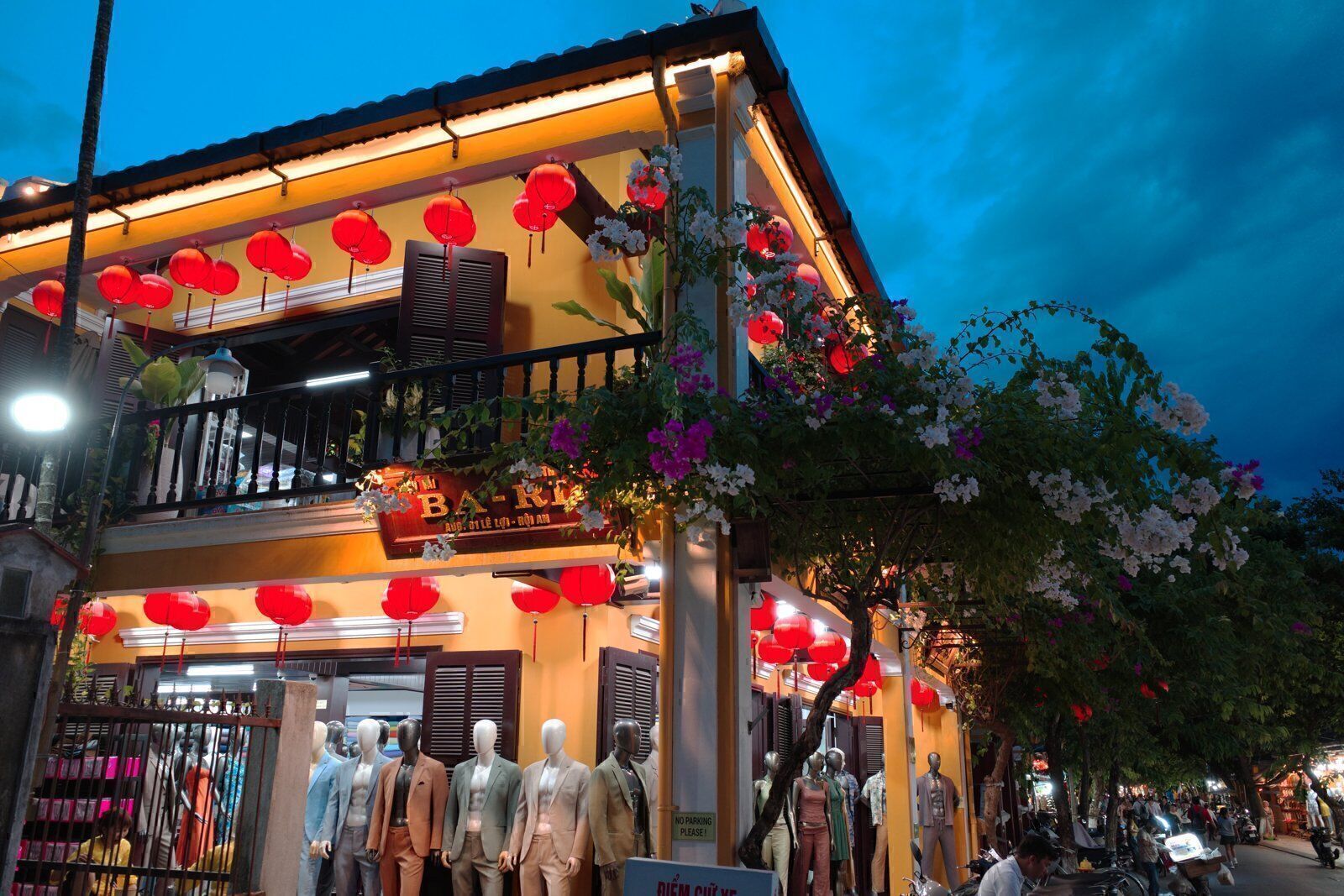 Hoi An tailor shop corner at blue hour with red lanterns, bougainvillea and mannequins outside