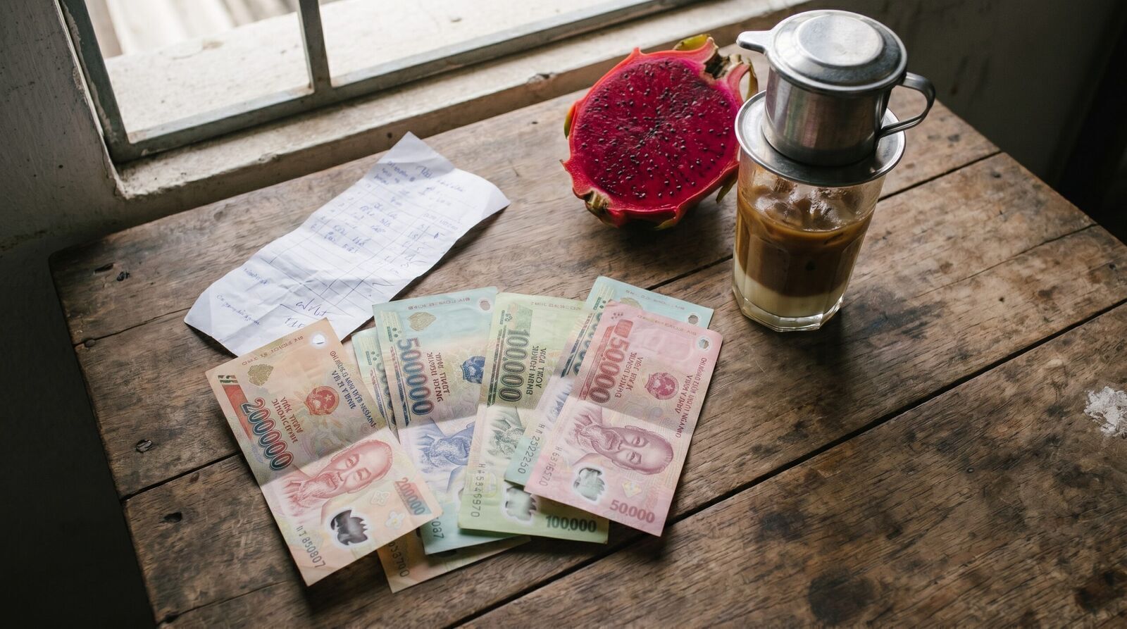 Vietnamese dong banknotes with receipt, iced coffee and dragon fruit on a wooden table