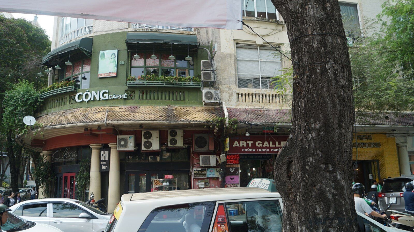 Green military-retro corner facade of a Cong Caphe branch on a tree-shaded Saigon street