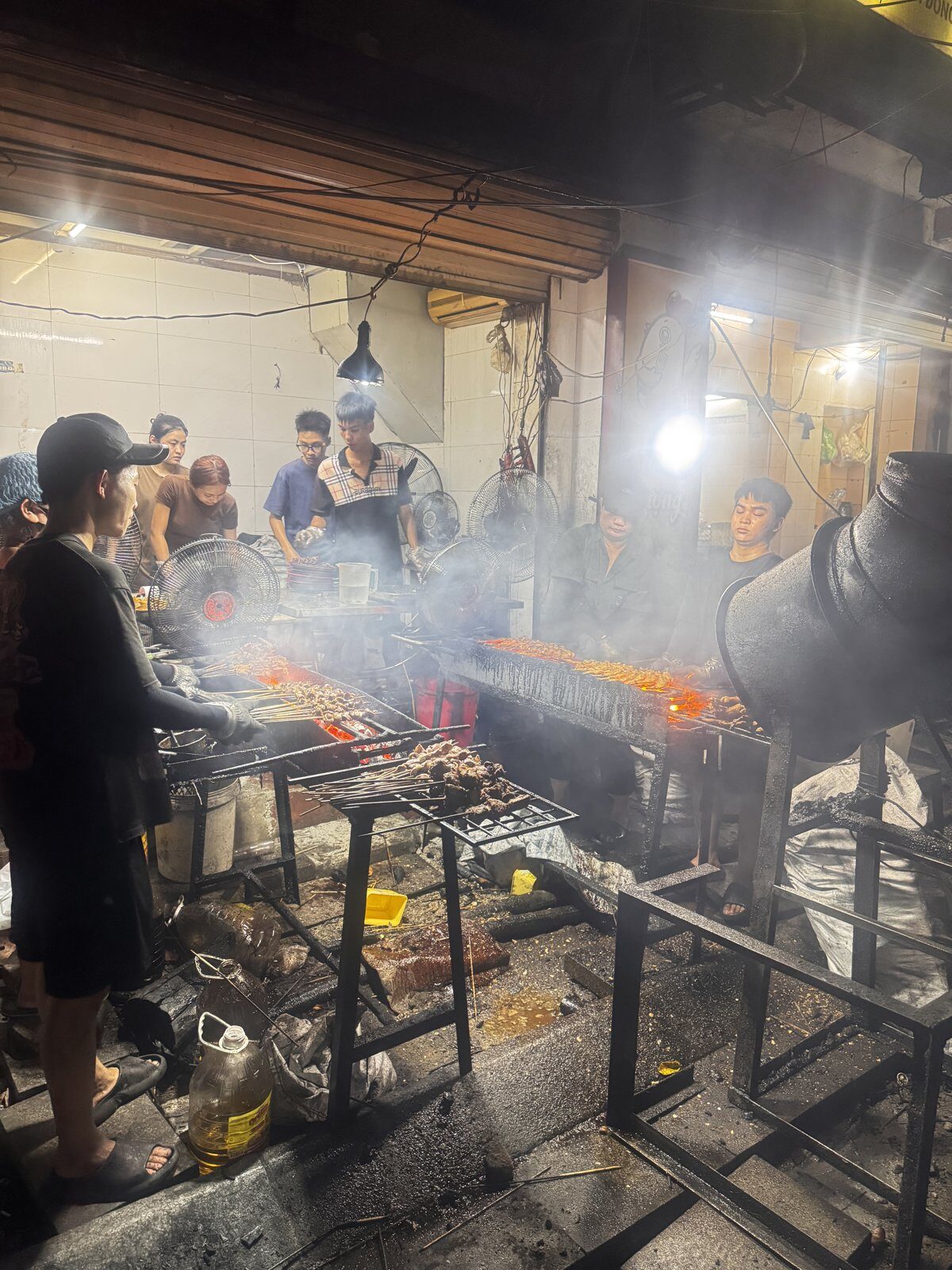 Skewers grilling over charcoal at a smoky Hanoi street barbecue at night