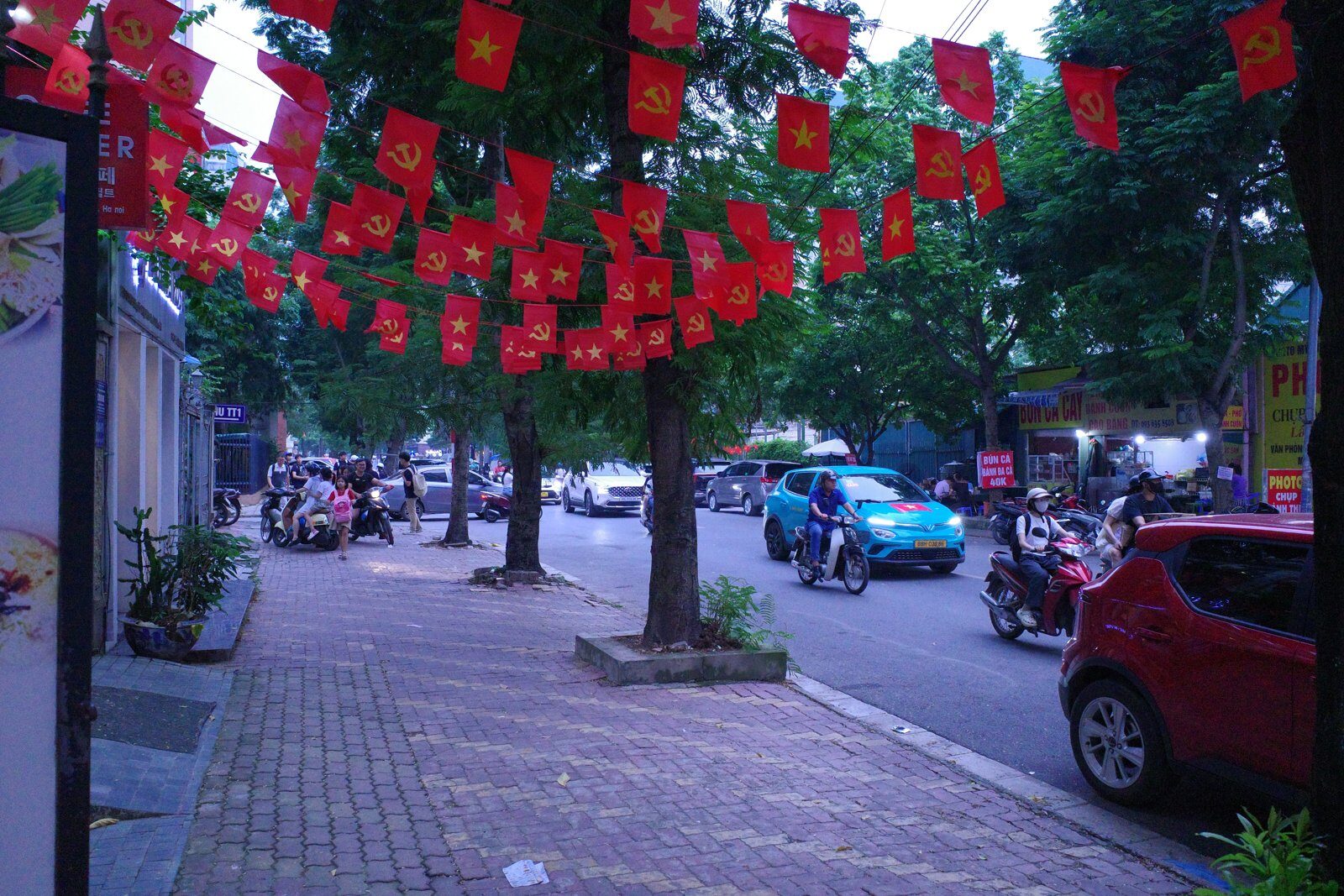 Hanoi street in early September draped with red national and party flags, motorbikes and a taxi passing