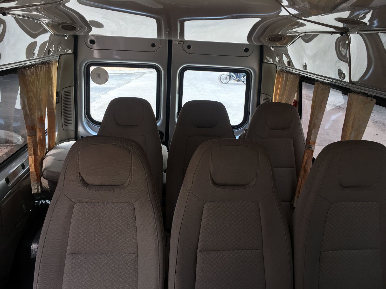 Inside a 16-seat Ford Transit limousine van in Vietnam: wide fabric seats, curtains and a motorbike passing outside the rear window