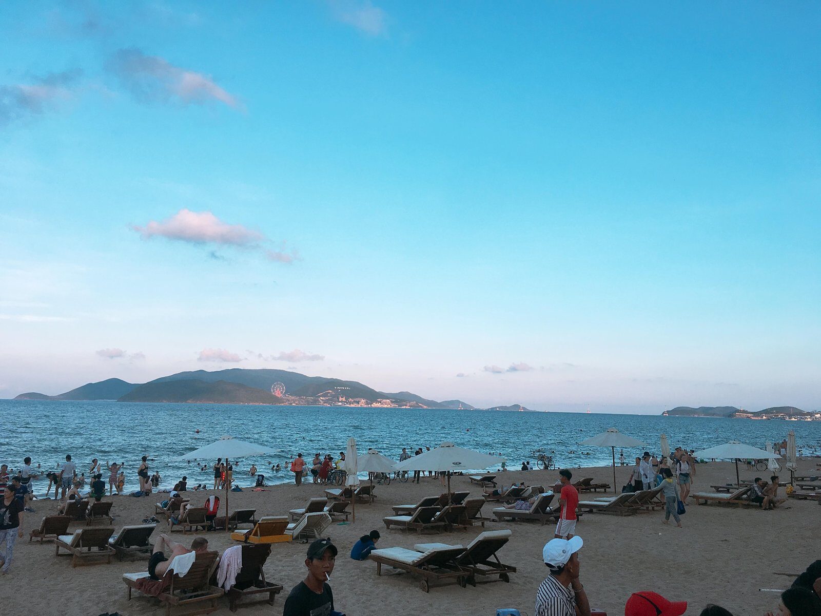 Nha Trang municipal beach at dusk with sun loungers, umbrellas and mountains across the bay