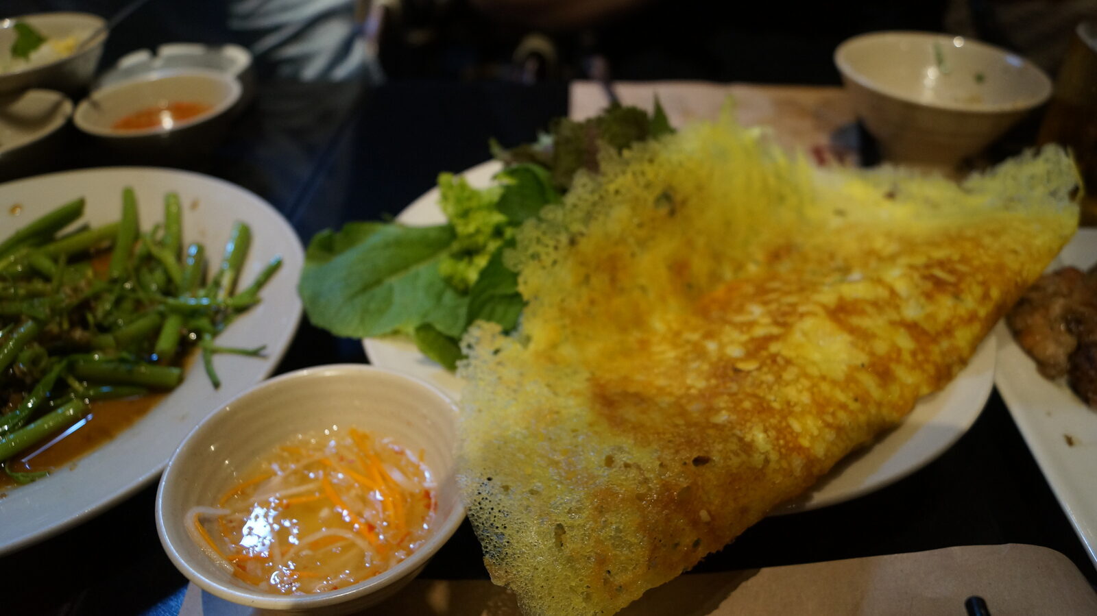 Banh xeo turmeric crepe with lacy crispy edge, greens for wrapping and nuoc mam dipping sauce in Saigon