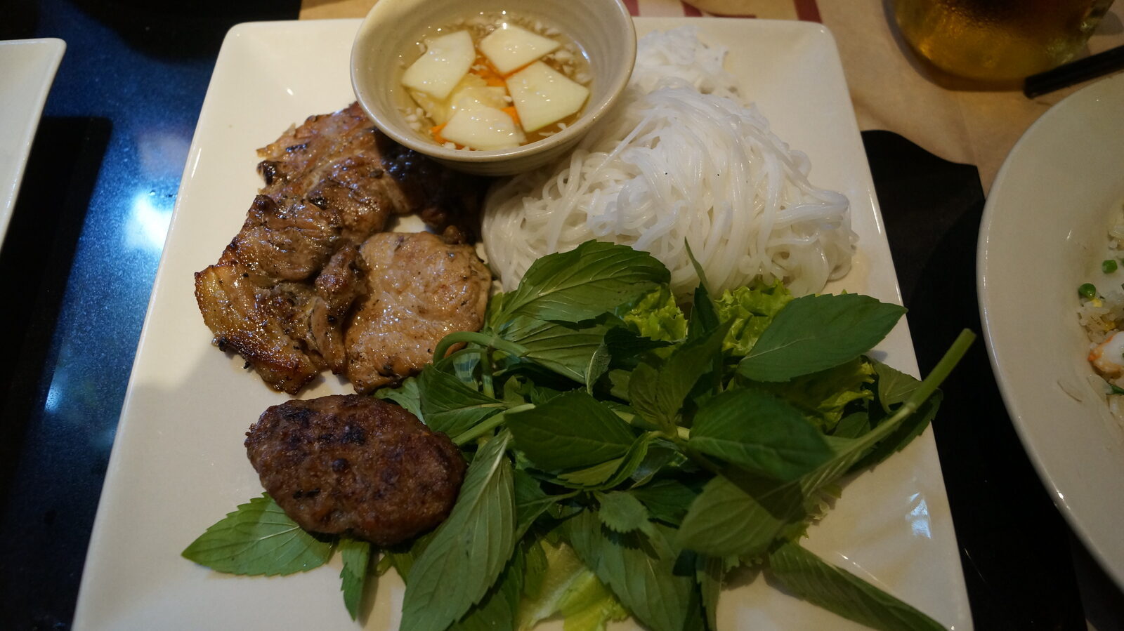 Charcoal grilled pork with rice noodles, fresh herbs and sweet fish sauce on a plate in Saigon