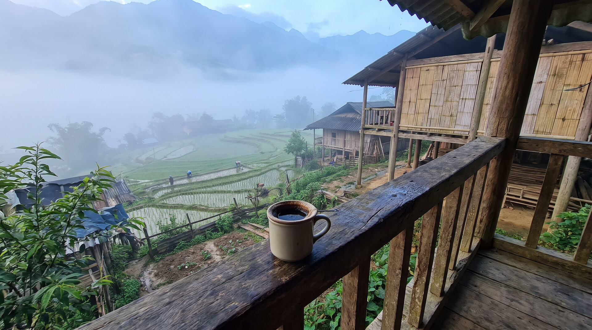 Morning fog lifting over rice terraces seen from a wooden homestay balcony in Ta Van village, Sapa Vietnam