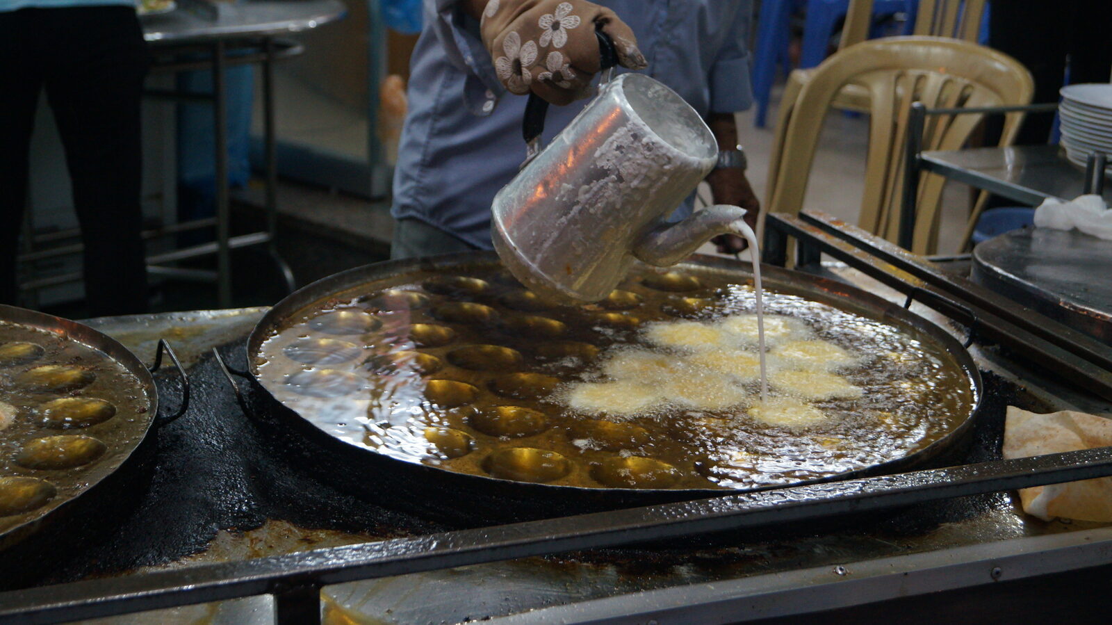 Banh khot batter being poured into a hot cast iron mold pan at a Vung Tau restaurant