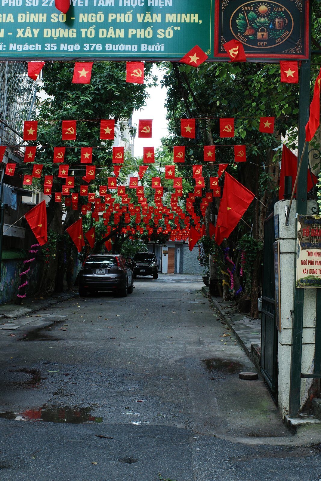 Narrow Hanoi alley hung with red lanterns and Vietnamese flags for National Day, cars parked along one side