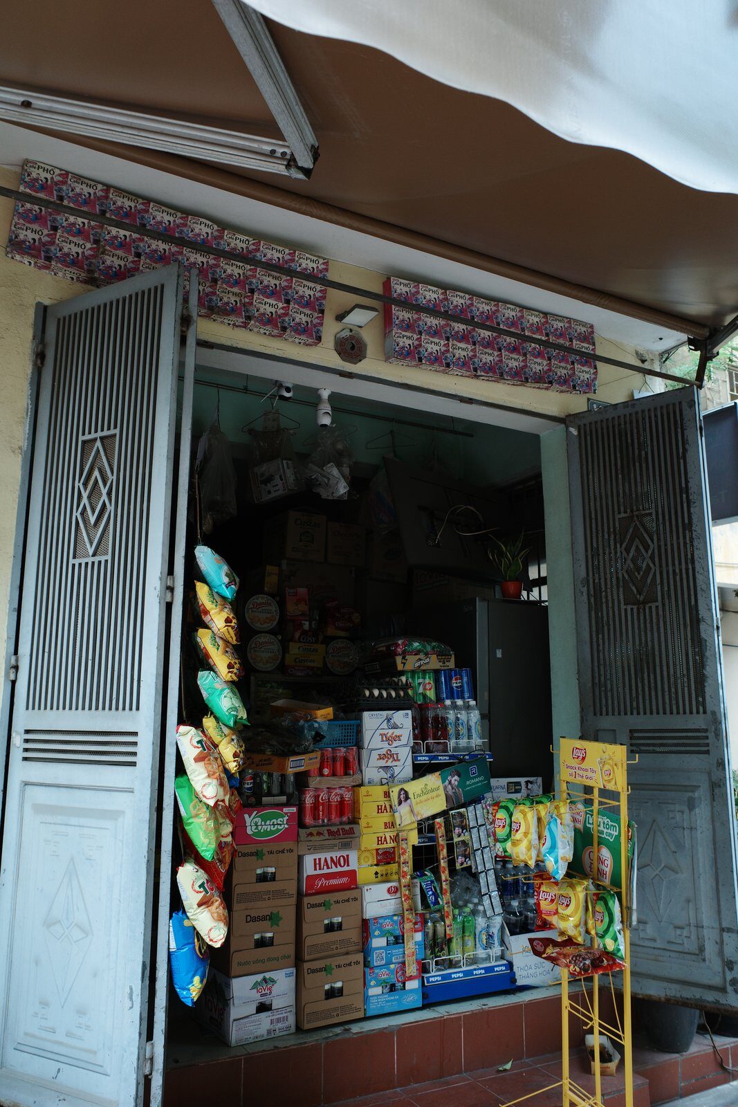A small Hanoi corner shop with shelves of snacks, drinks and household goods opening onto the street