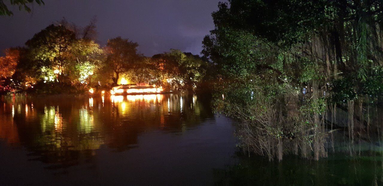 Hoan Kiem Lake in Hanoi at night in light drizzle, Turtle Tower lit up across the water and trees leaning over the shore