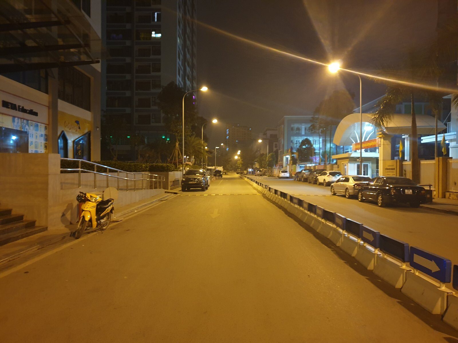 An empty six-lane road in Hanoi at night under orange streetlights, three nights before Tet, with one parked motorbike