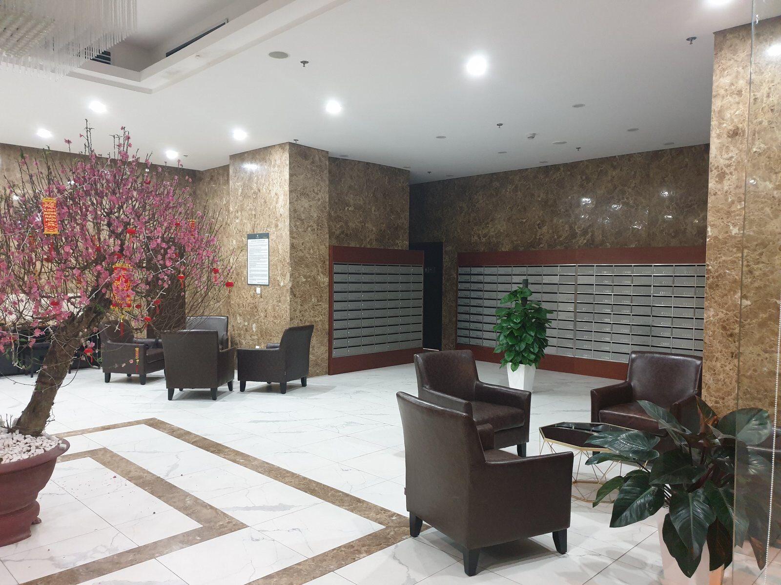 A large pink peach blossom tree with red lucky-money envelopes hanging from its branches in a marble apartment lobby in Hanoi before Tet
